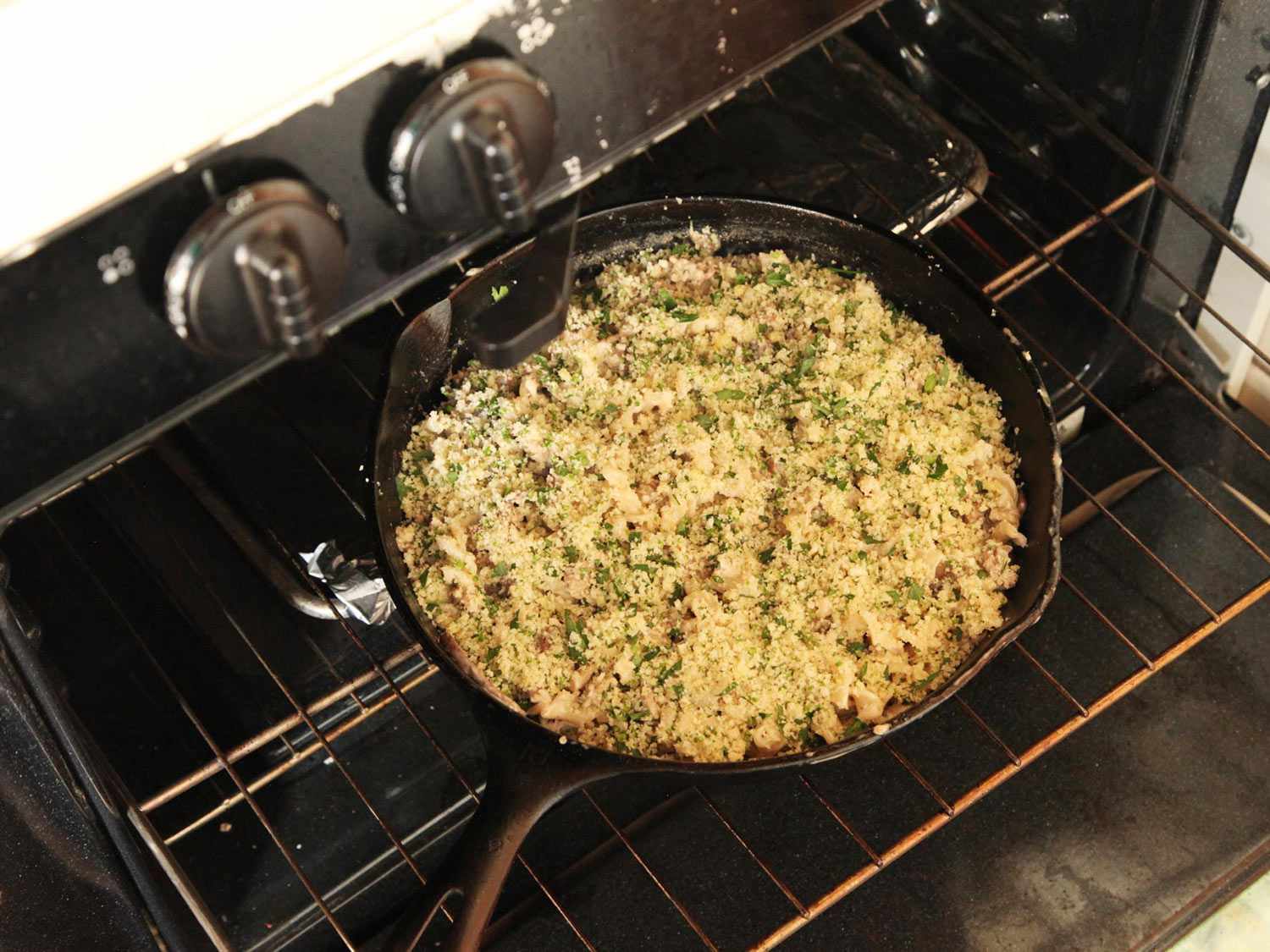 Transferring a cast iron skillet containing pasta in mushroom sauce with sausage to bake. 