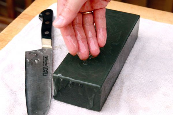 Hand feeling a whetstone on a towel set on a cutting board