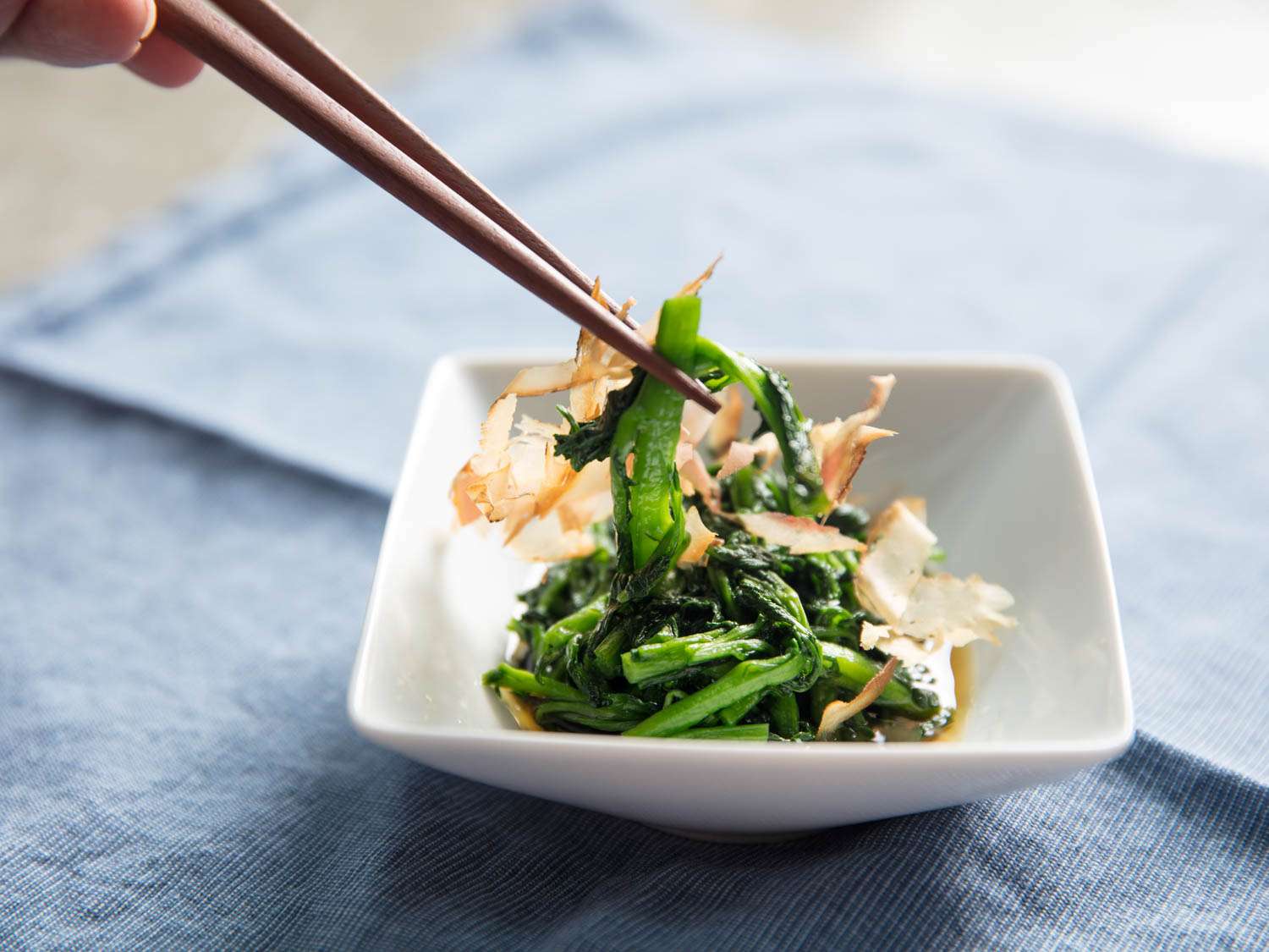 Chopsticks picking up some marinated spinach with shaved bonito.