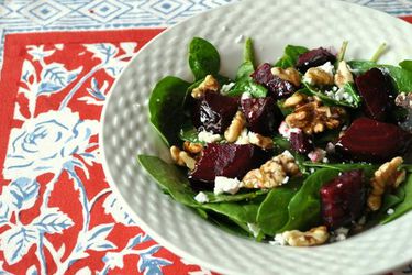 Closeup of spinach salad with beets and walnuts, served in a bumpy-rimmed bowl.