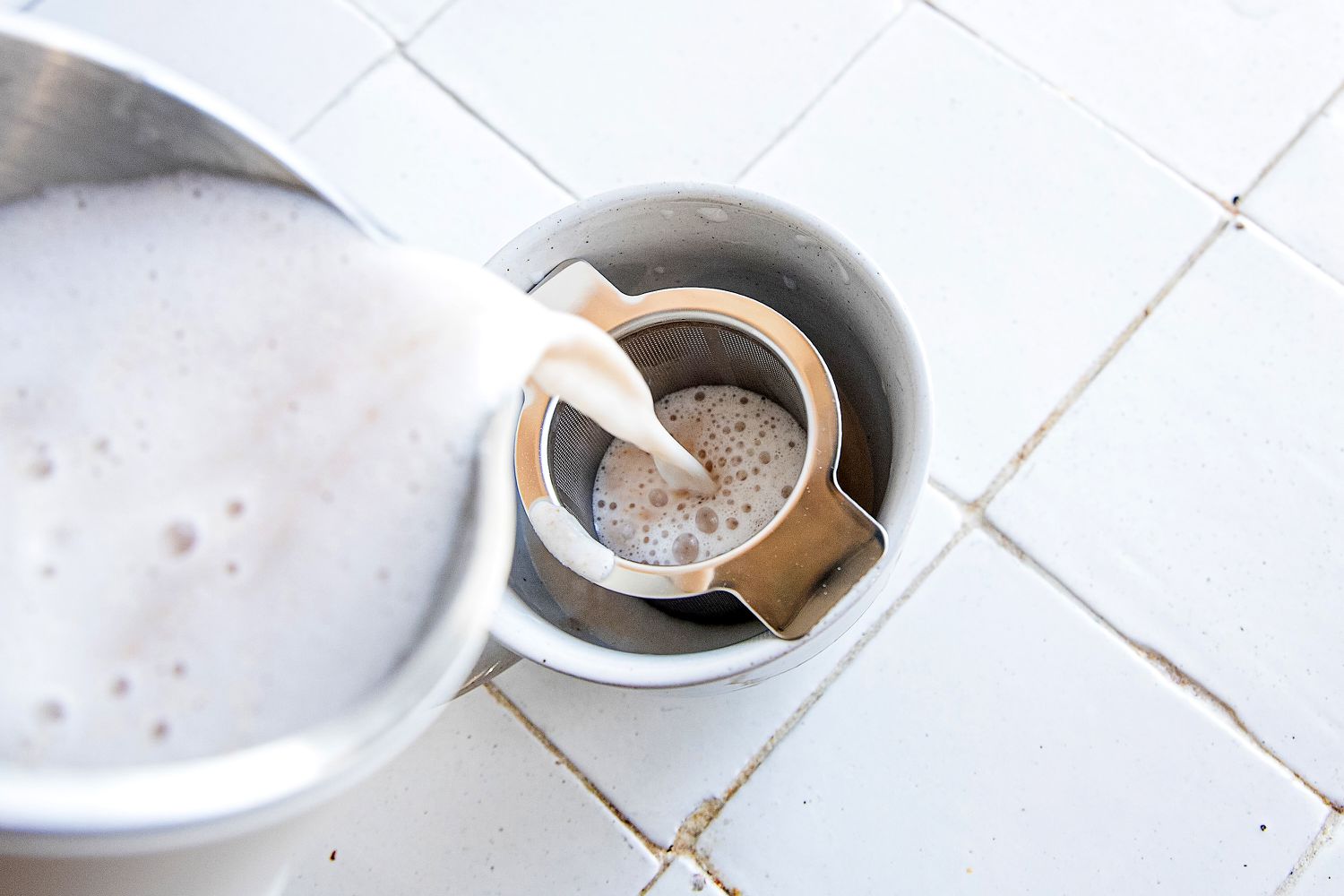 pouring the blended almonds and water from the alfabot into a strainer