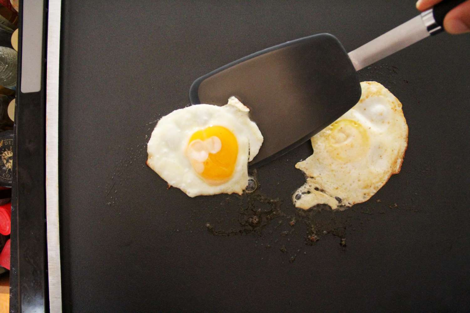 A black metal food turner lifts a fried egg from a griddle