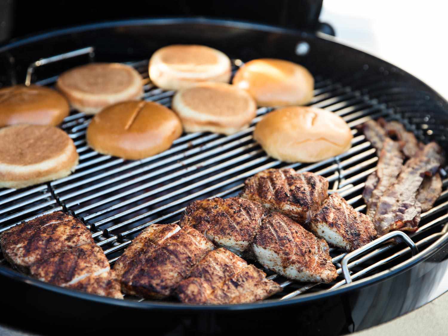 The blackened fish fillets and bacon are moved to the periphery of the grill to make way for toasting bun halves, cut side facing down.