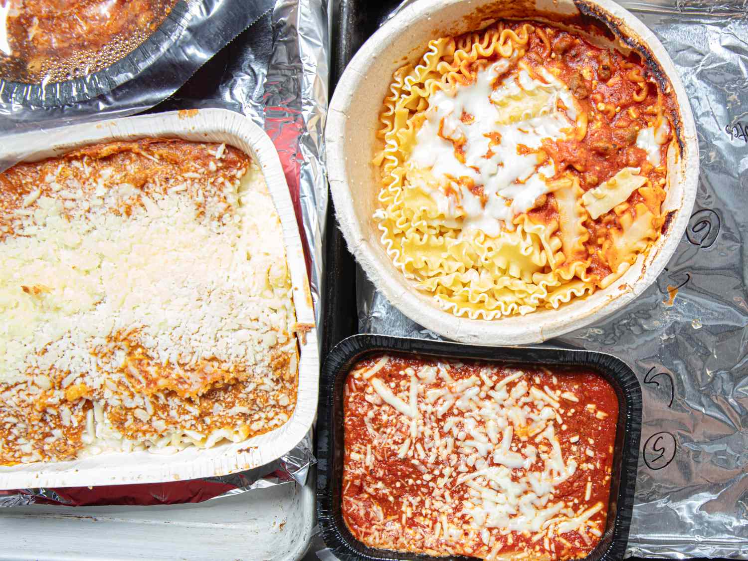 Four dishes of frozen lasagna displayed on a reflective surface showcasing variations in preparation and presentation
