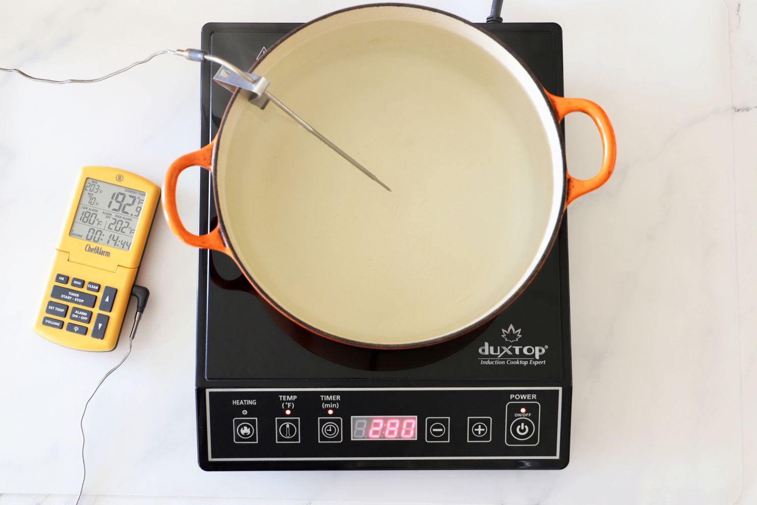 A cooking pot on a Duxtop induction burner with a thermometer probe inserted and a digital thermometer placed nearby