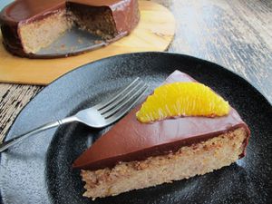 Closeup of a slice of Hazelnut Chocolate Torte With Espresso Ganache served on a black plate, topped with an orange suprême.