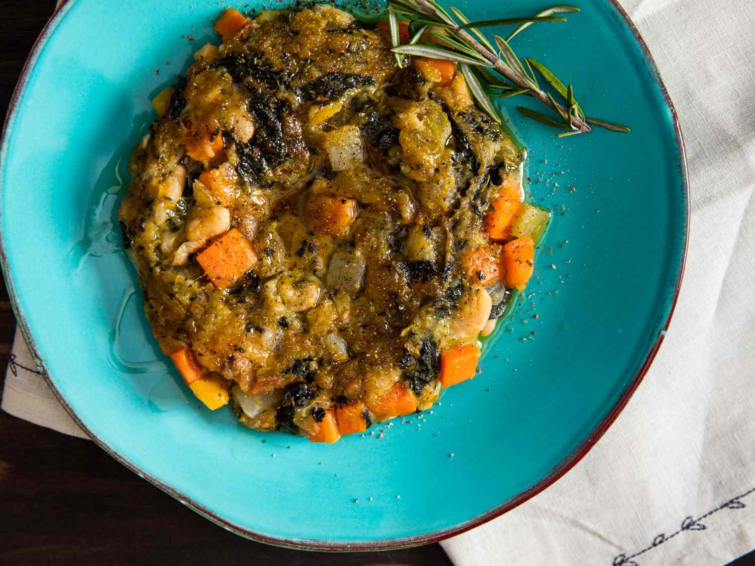 Overhead view of a plated ribollita pancake, garnished with a sprig of fresh rosemary and a few grinds of black pepper.