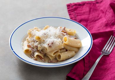 A white bowl of Pasta alla Gricia topped with shredded cheese