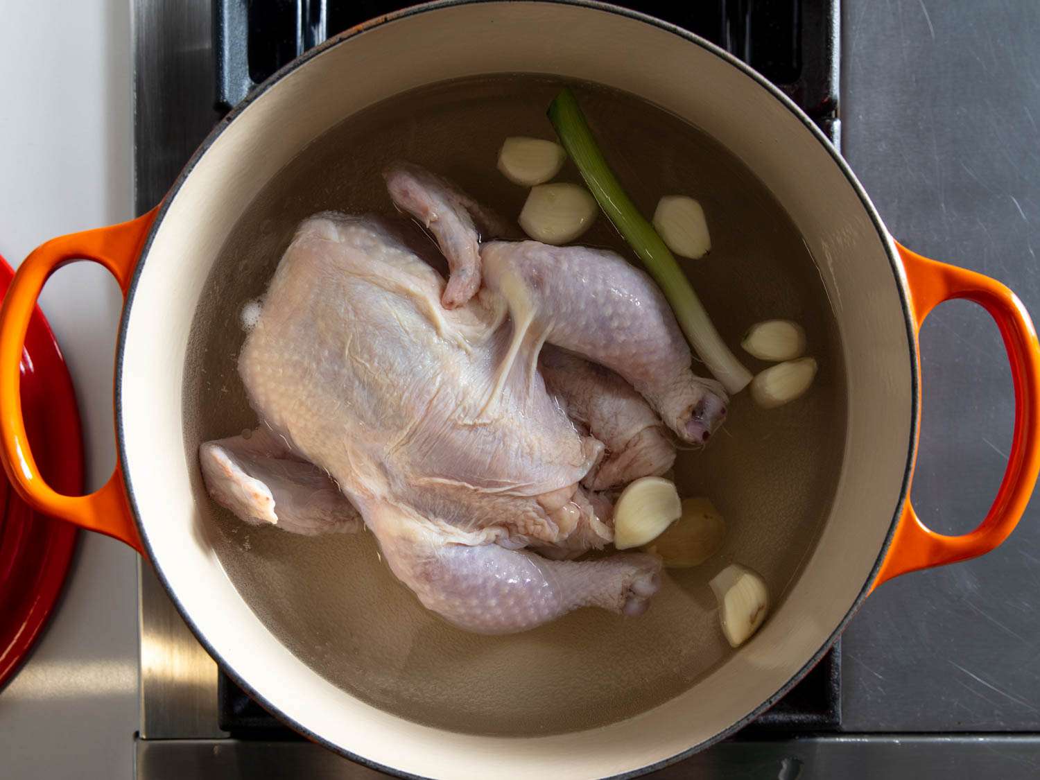A whole raw chicken in a pot with water, garlic, and green onion.