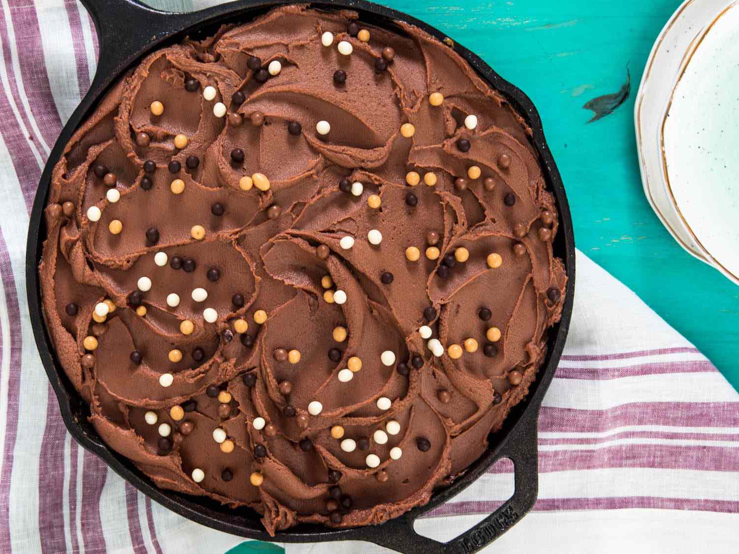 Overhead shot of a frosted chocolate skillet cake, topped with chocolate pearls.