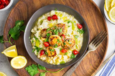 Overhead view of a dark gray bowl containing seared sea scallops with leek risotto and lemon-brown butter sauce.