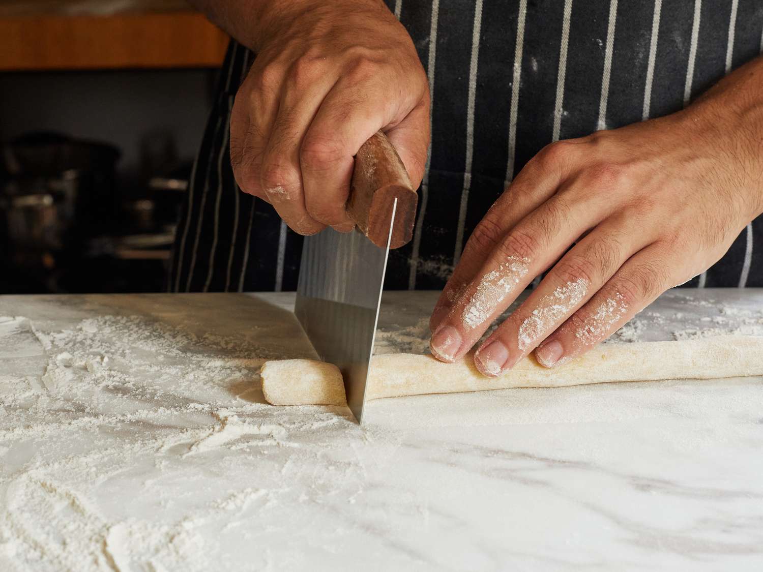 a person using a bench scraper with a wooden handle to slice pieces of gnocchi