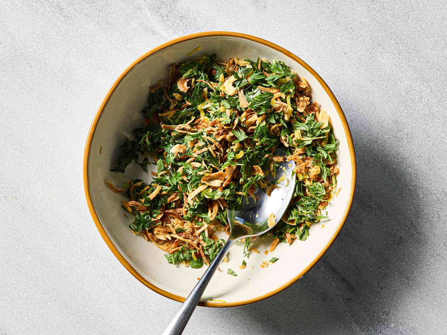 A bowl containing herbs and crispy fried garnishes, shown with a spoon