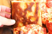 A person showing the underside of a pizza made in the LloydPans Kitchenware 10 by 14 Inch Detroit Style Pizza Pan