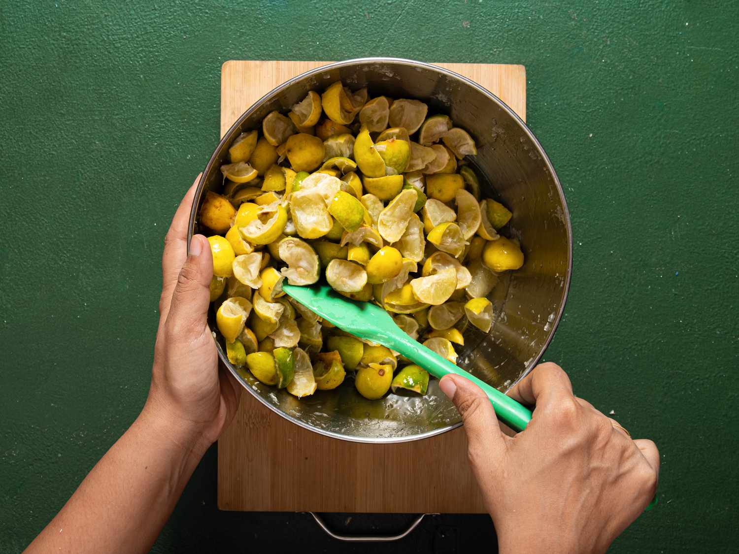 Hands mixing lemon slices in a bowl with a green spatula
