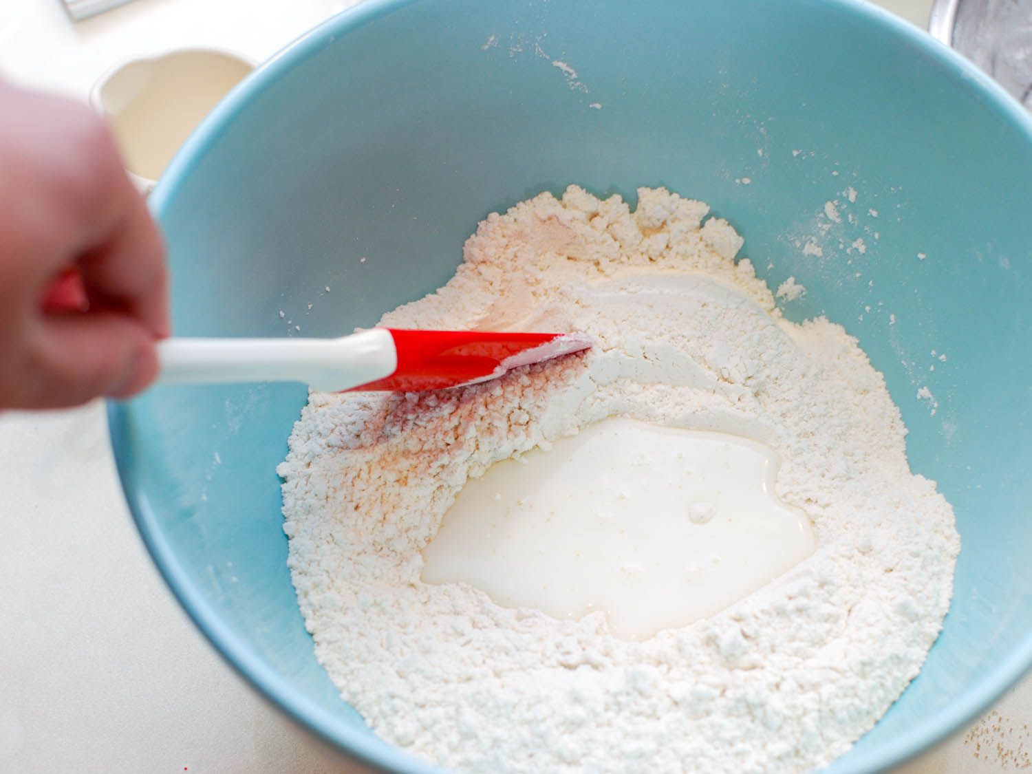 The dry ingredients for sheng jian bao dough are mixed in a blue prep bowl with a flexible spatula.
