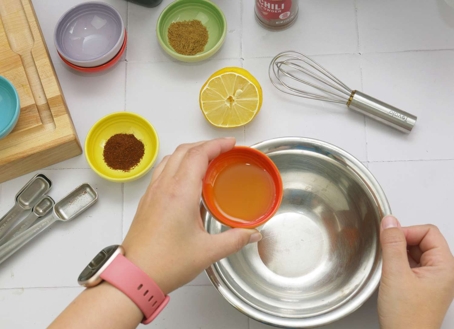 a person pouring oil out of an orange pinch bowl into a metal bowl