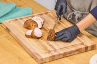 Person slicing cooked meat on a John Boos Reversible Maple Wood Cutting Board with Juice Groove