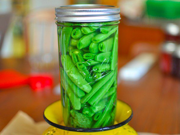 Closeup of a sealed glass jar of pickled sugar snap peas set on top of inverted yellow colander