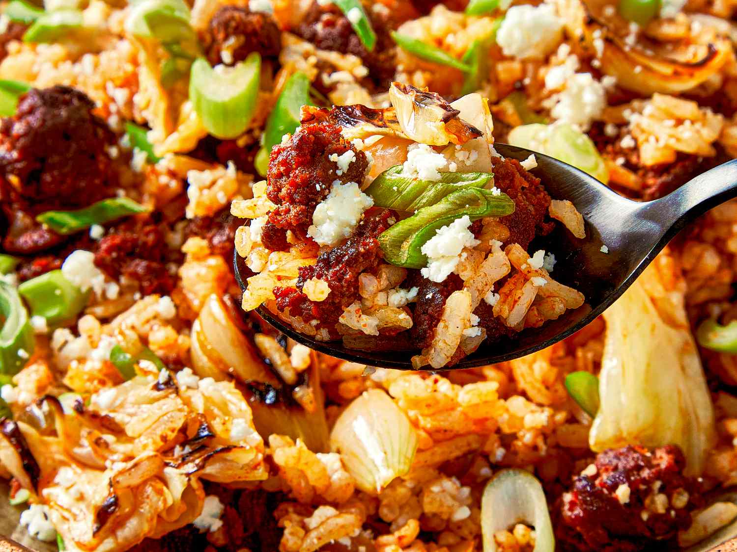 Mexicaninspired fried rice served with toppings including green onions and crumbled cheese on a spoon
