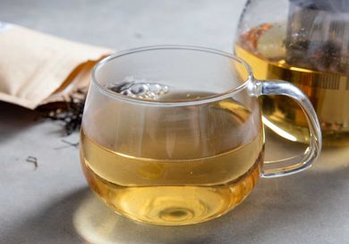 A handled glass cup of black tea from The Great Mississippi Tea Company, with loose-leaf black tea and a carafe of tea in the background