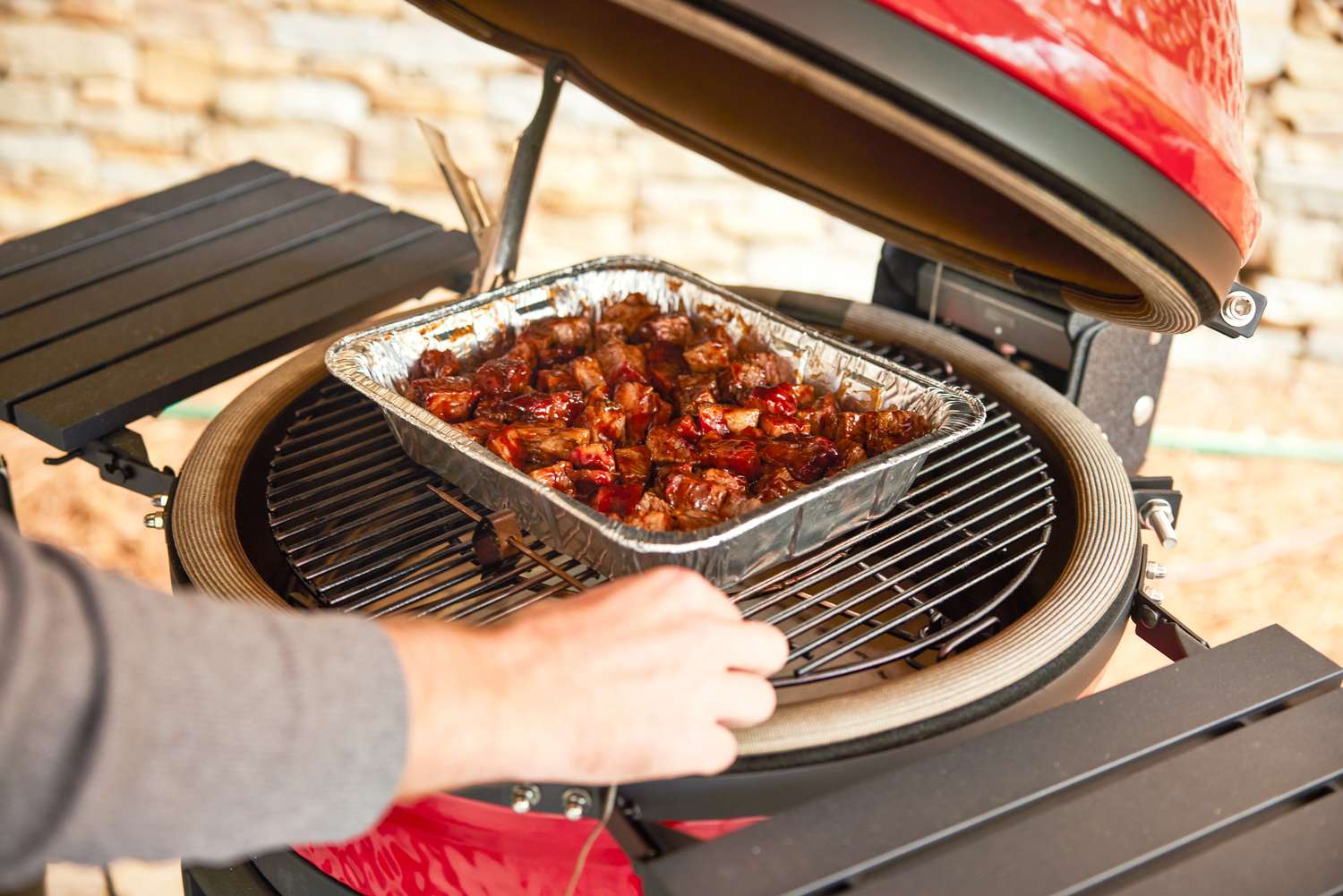 a person setting an aluminum tray of food onto the Konnected Joe's grate