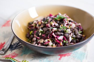 A beige bowl of bean salad with radicchio, radish, pickled onions, and almonds.