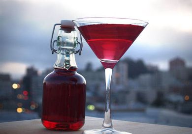 A bottle of DIY grenadine sits next to as large martini glass filled with a grenadine-tinged cocktail.