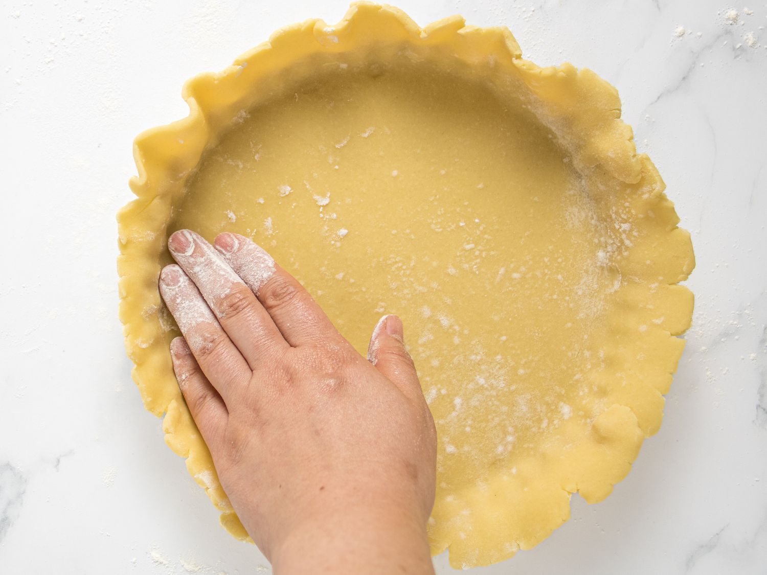 Floured hand pressing dough into the edges and bottom of pie pan 