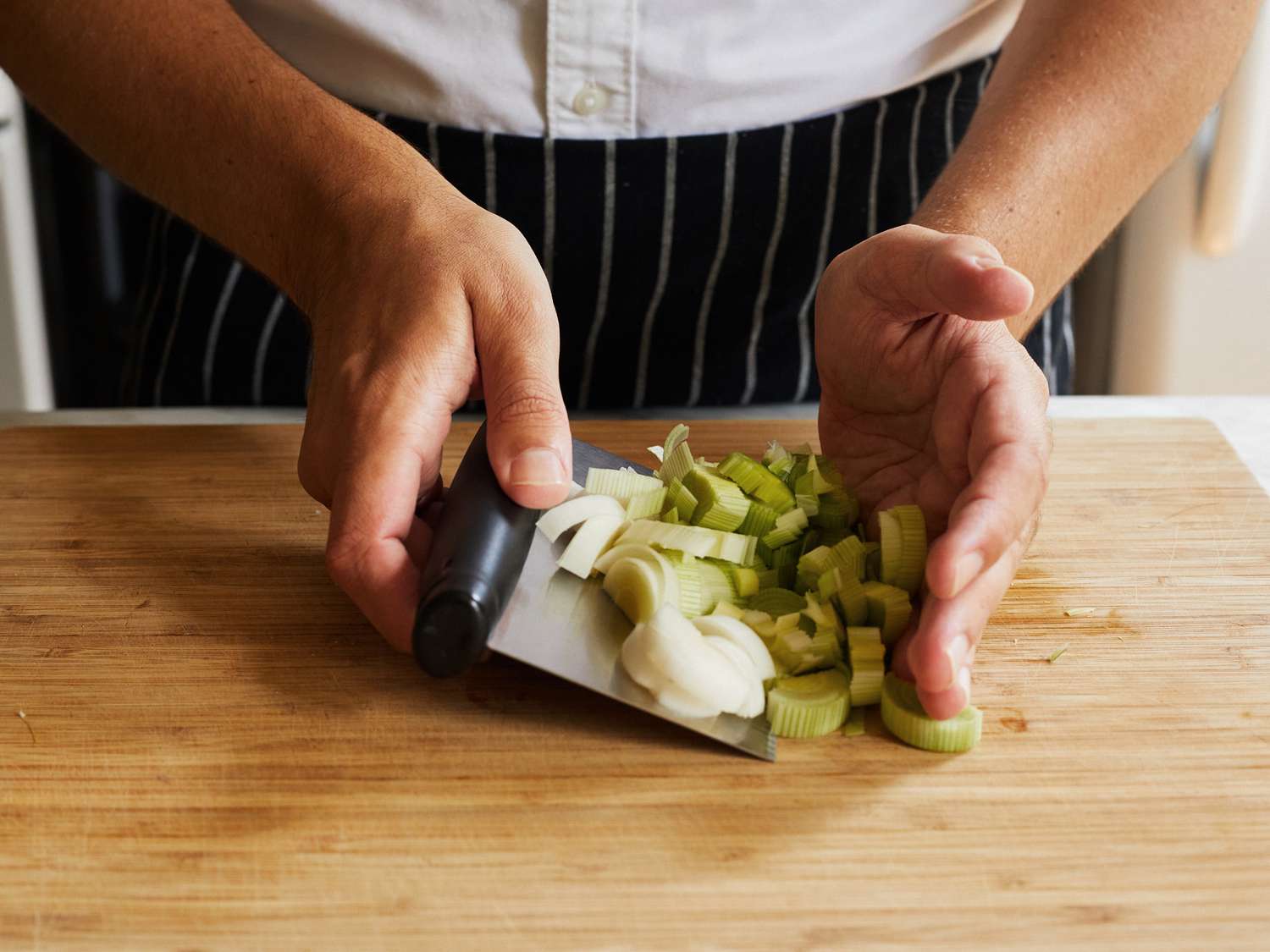 A cook uses a bench scraper to transfer chopped leeks