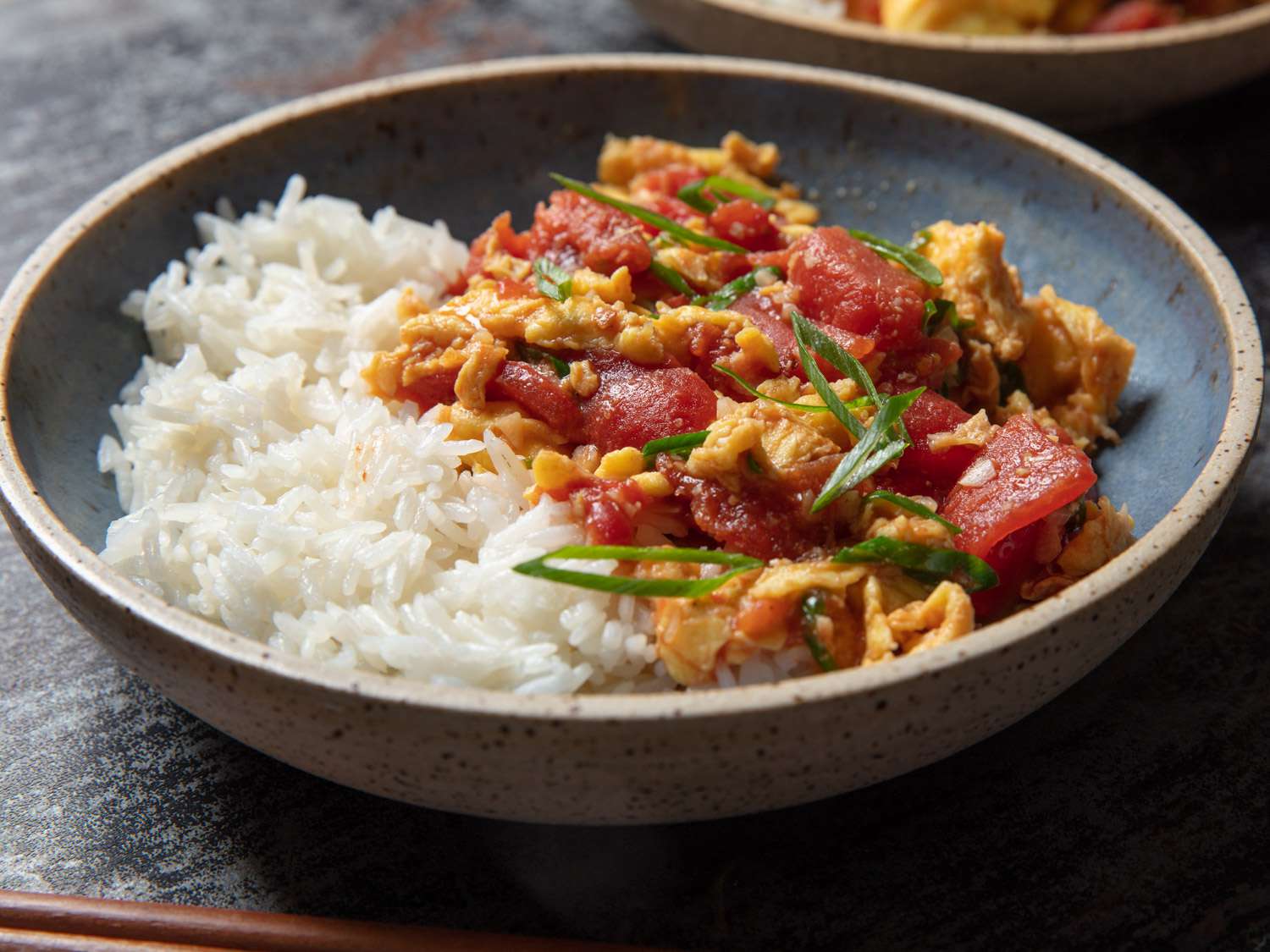 Tomato and eggs plated in a ceramic bowl with rice.