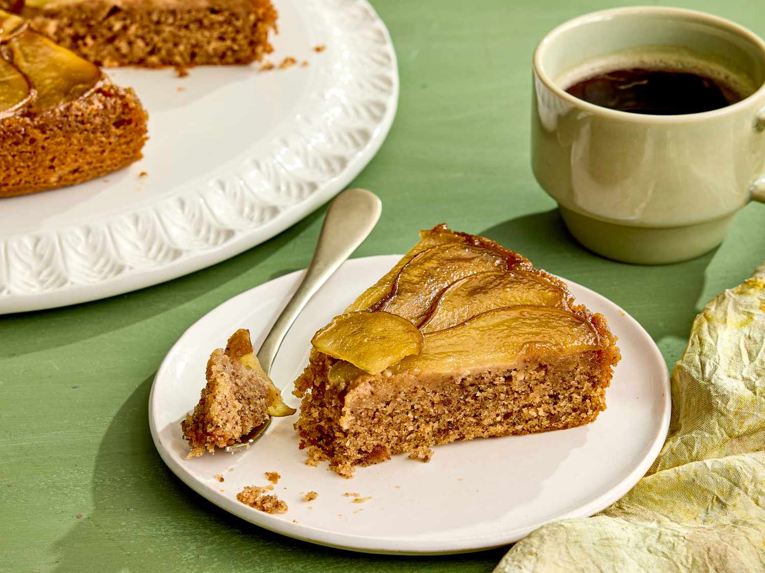 Slice of pear upsidedown cake on a plate with a cup of coffee