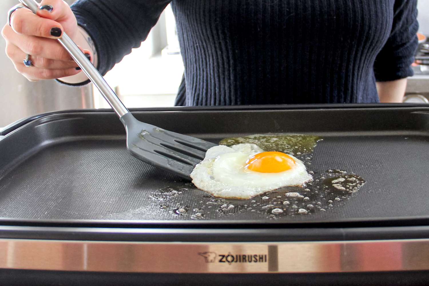 A person using the Tovolo Silicone Slotted Turner to flip an egg