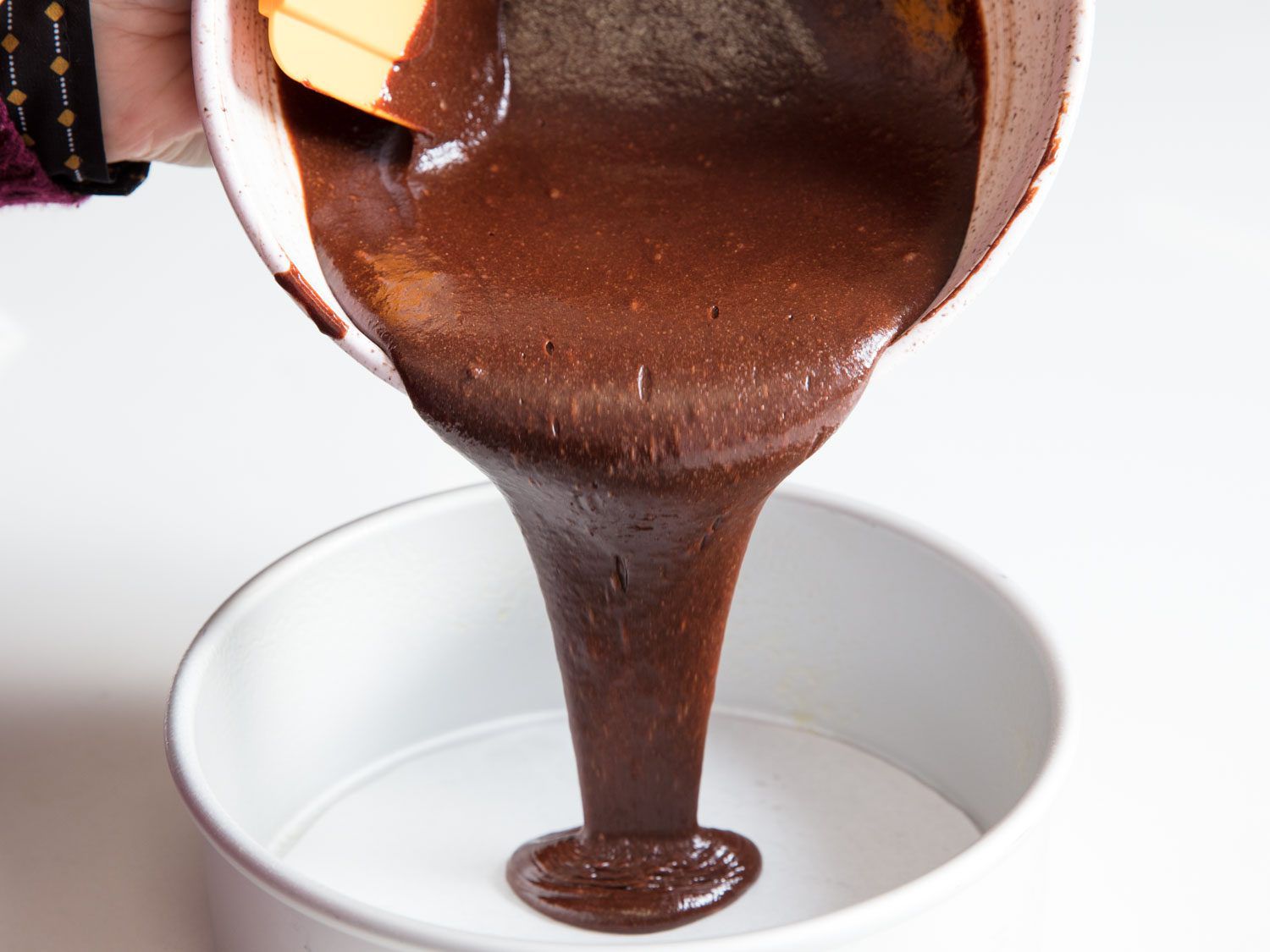 Pouring the dairy-free chocolate cake batter into a round cake pan.