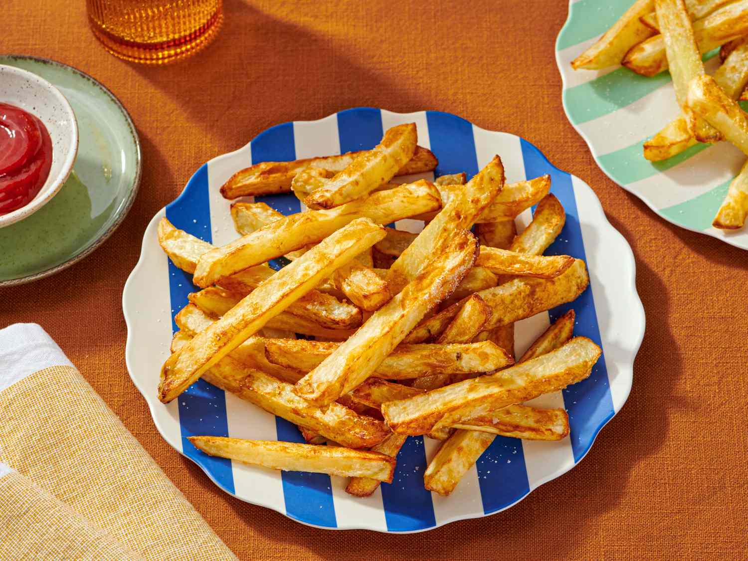 A plate of French fries on a striped plate next to a cup of ketchup