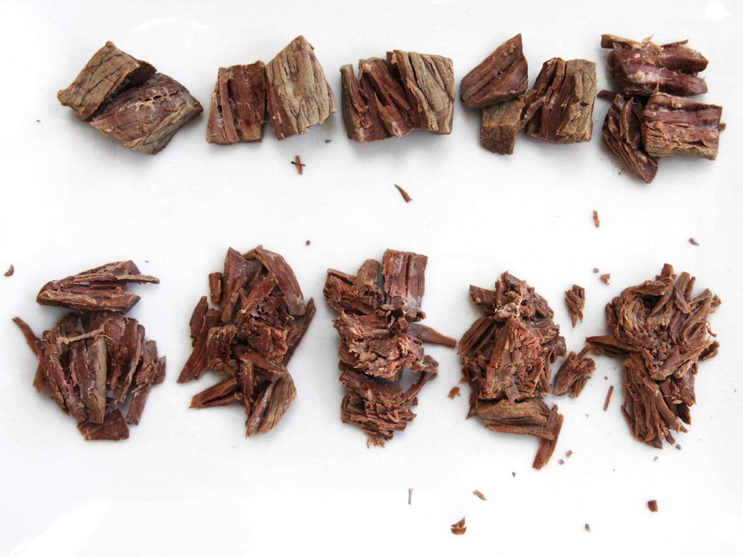 Cooked cubes of beef arranged on a white surface according to how long they were cooked. The cubes have been compressed with a standard amount of weight. Those cooked for longer have disintegrated and broken apart into stringy fibers under the pressure.