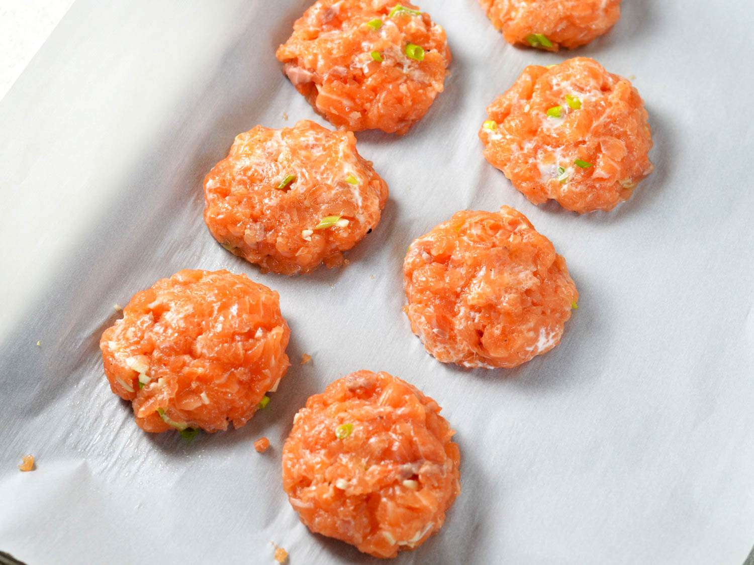 Row of raw mini salmon burgers patties on parchment paper