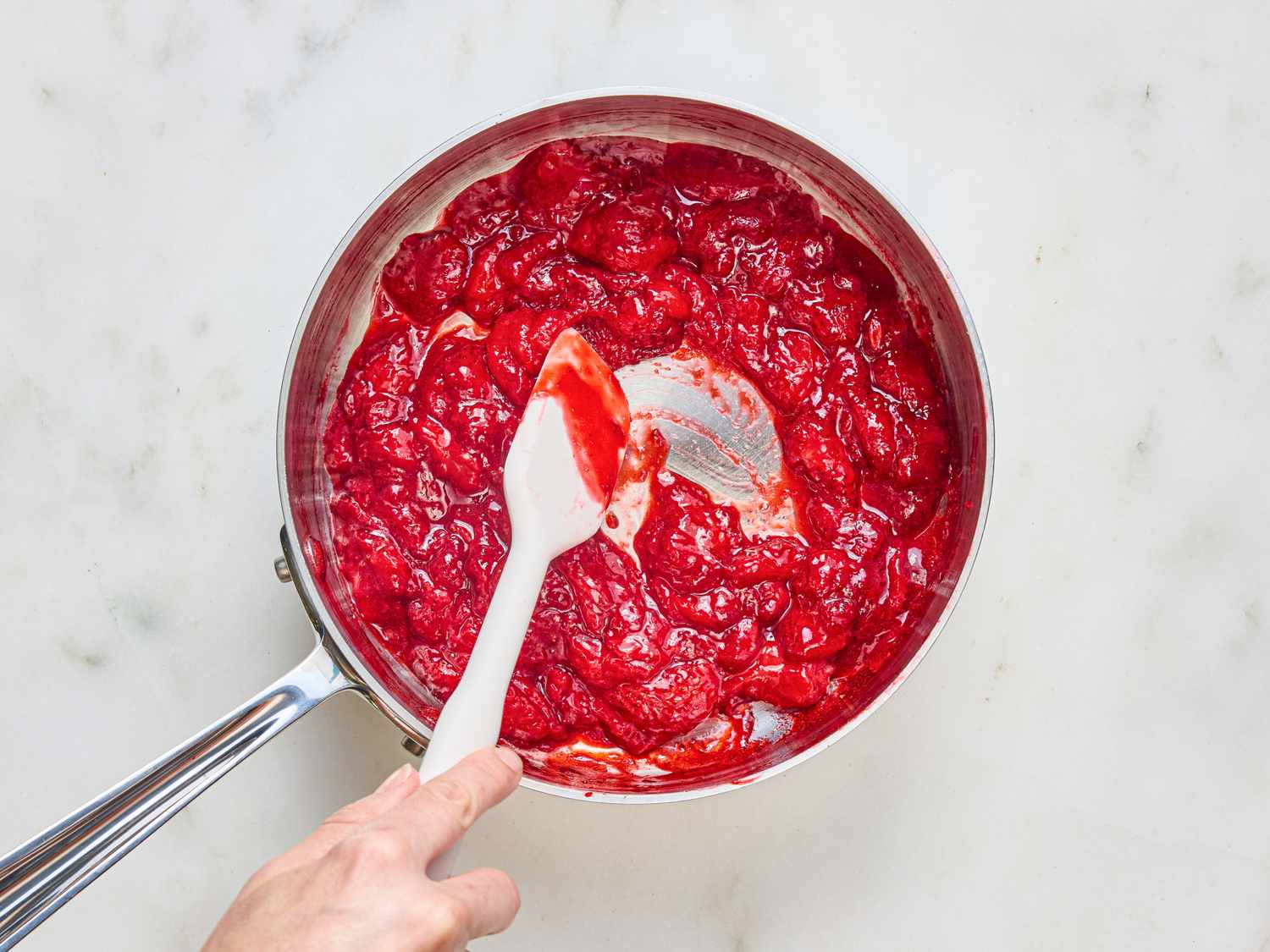 A pan of cooked strawberry mixture being stirred with a white spatula