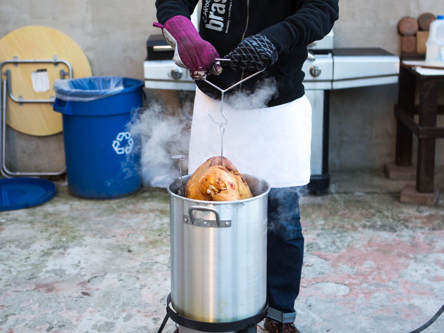 A person lifting a deep fried turkey out of kettle of boiling oil