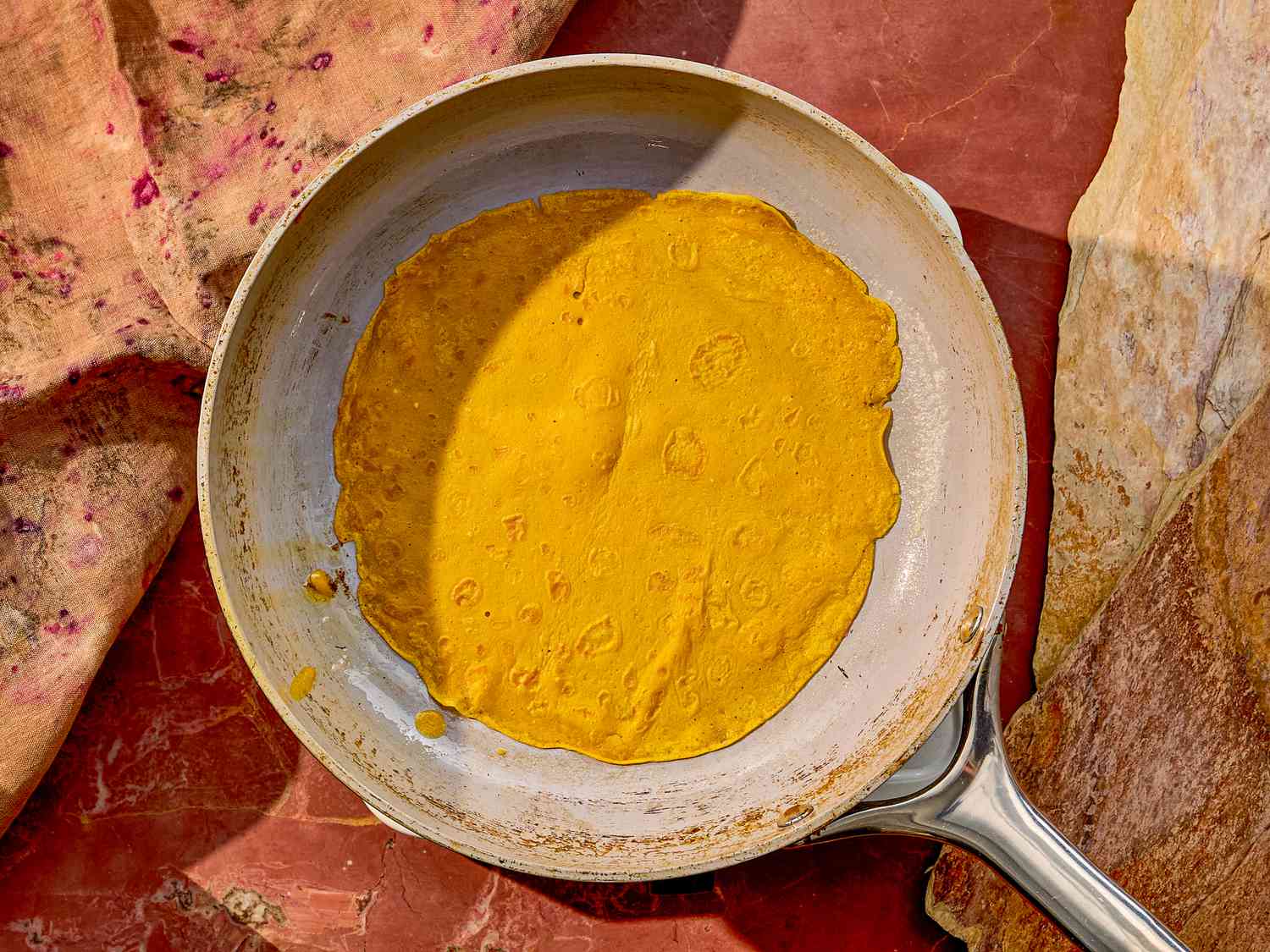 A crepe cooking in a pan on a countertop with surrounding crêpes