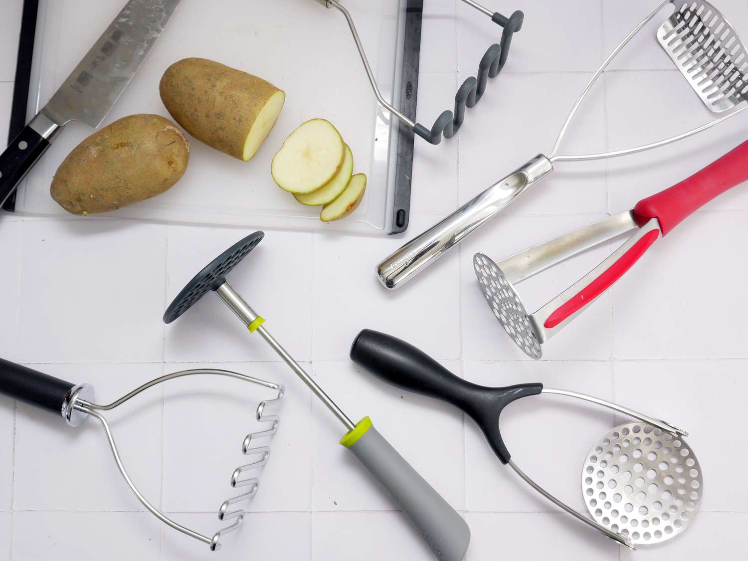 potato mashers on a white backdrop with a sliced potato and cutting board