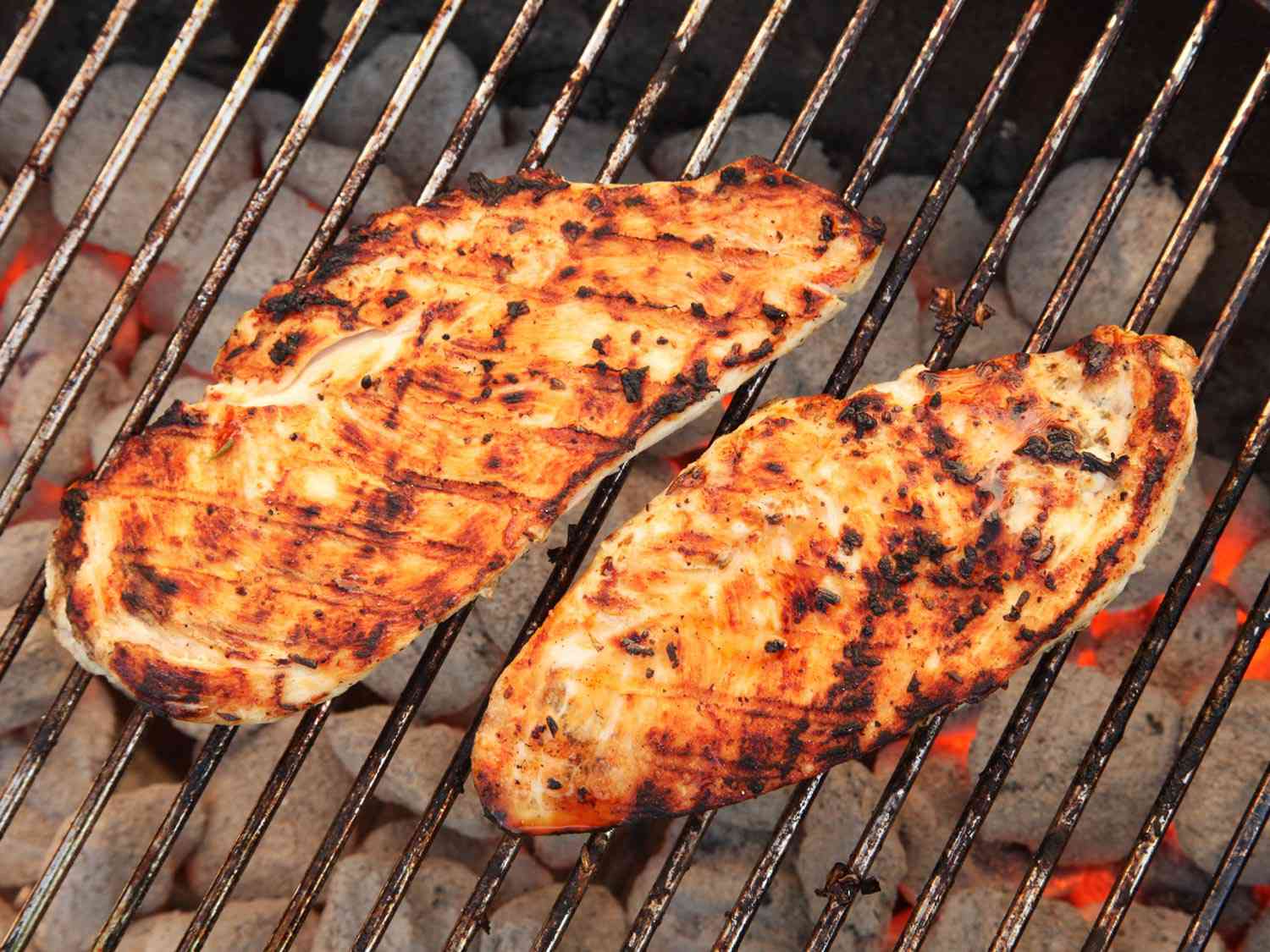 Two seasoned chicken cutlets with char marks on a hot grill. 