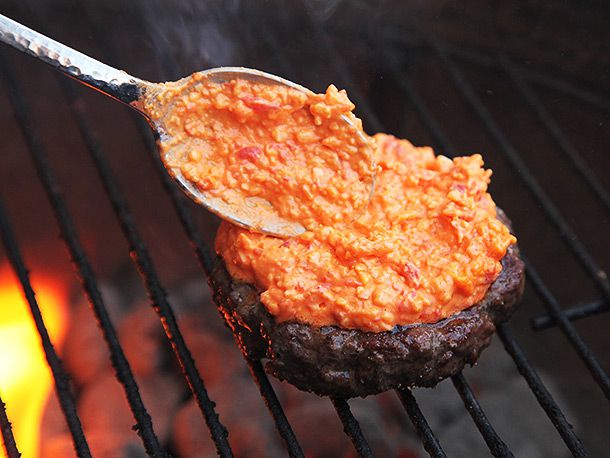 Adding pimento cheese on top of a burger on a grill.