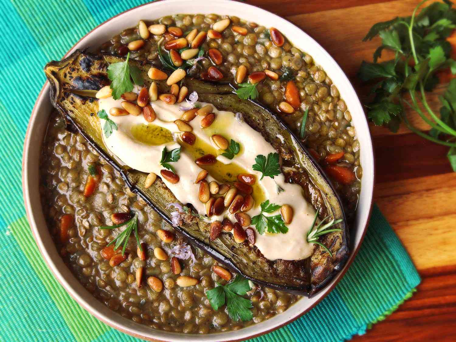 The finished dish, with the roasted eggplant draped atop the stewed lentils. Tahini sauce, toasted pine nuts, and cilantro and rosemary leaves garnish the dish.