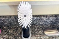 A closeup of an OXO dishwashing wand in a plastic holder next to a kitchen sink