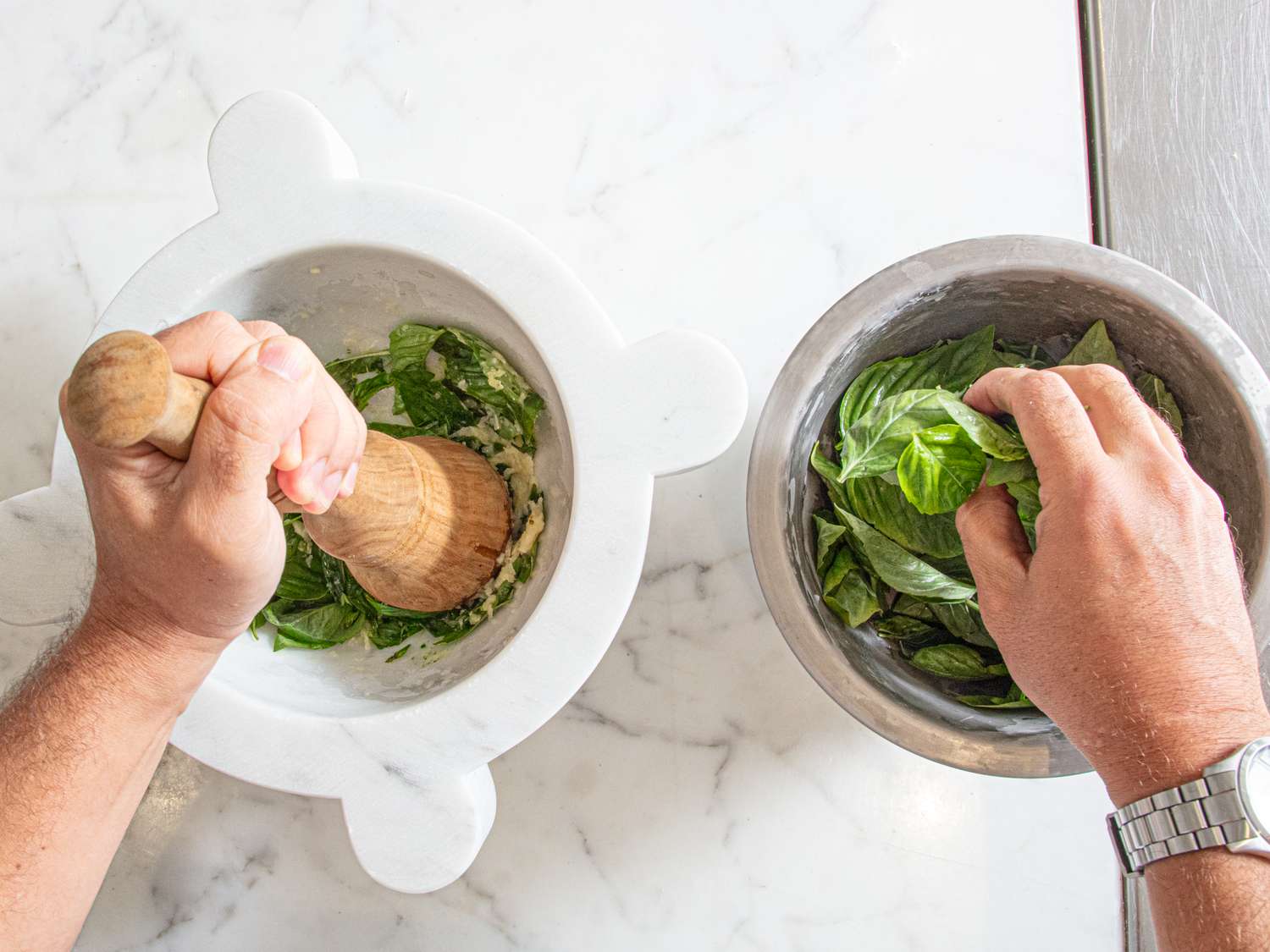 Hands preparing pistou using a mortar and pestle and a bowl of basil leaves