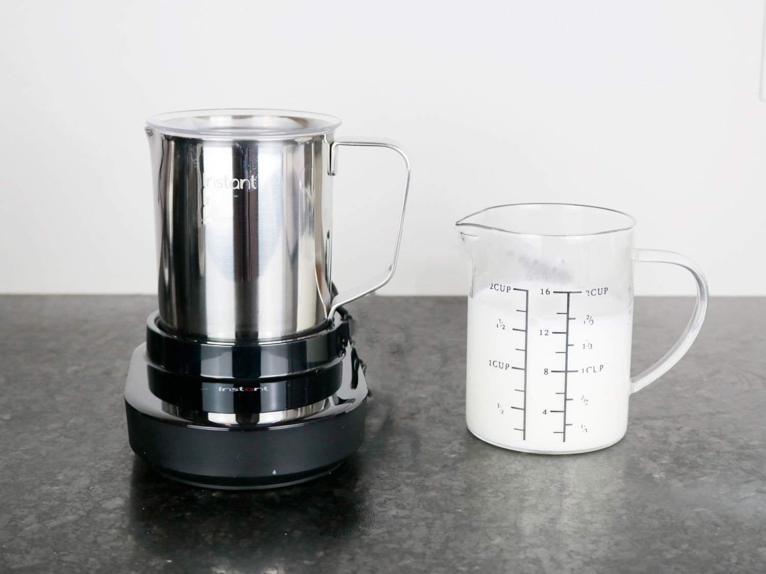 The Instant milk frother beside a glass pitcher holding frothed milk.