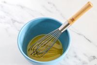 A whisk in a blue Bamboozle bowl containing a liquid mixture on a marble surface