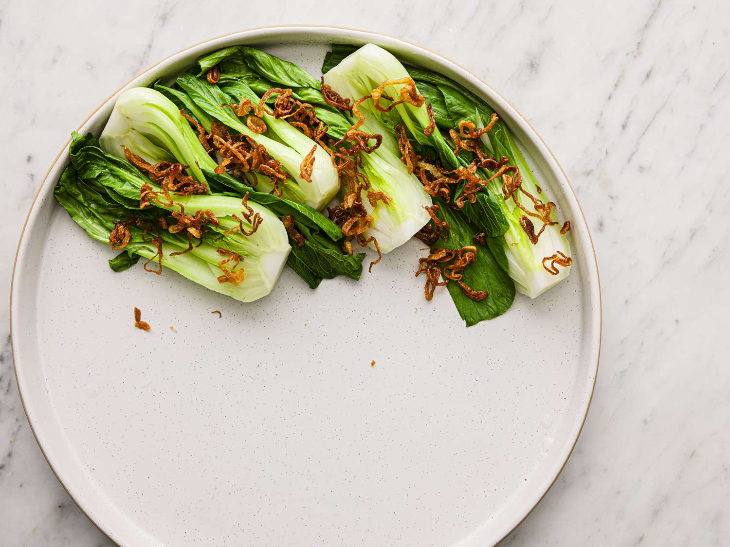Bok choy cooked and sprinkled with fried shallots on a plate