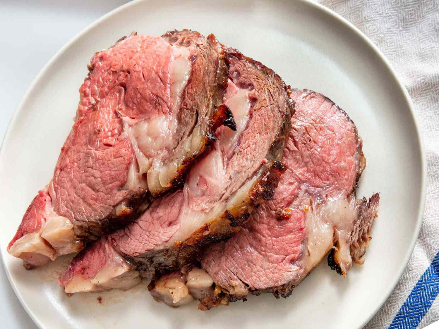 Closeup overhead of three thick slices of koji prime rib on a serving plate.